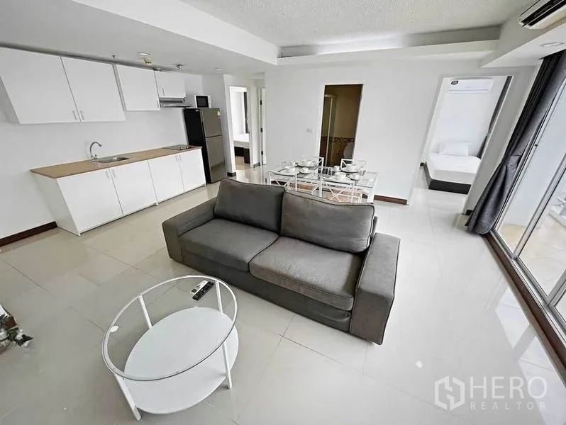 คอนโด ให้เช่าในKhlong Toei, Bangkok - มุมห้องนั่งเล่นเห็นครัว โต๊ะอาหาร โซฟาสีเทา และหน้าต่างสูงจรดเพดาน