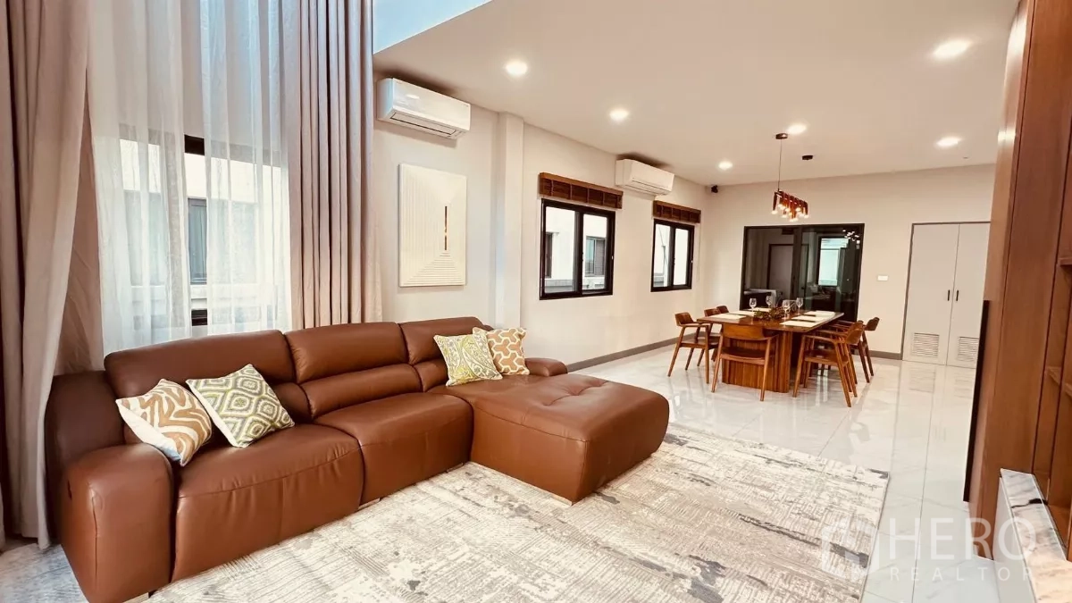 Detached House for rent in Bang Phli, Samut Prakan - Spacious lounge with a brown sectional sofa, multiple windows and recessed lighting.