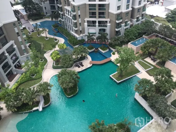 Condominium for rent in Huai Khwang, Bangkok - Aerial view of a resort-style lagoon pool with landscaped gardens, bridges and modern condominium towers.