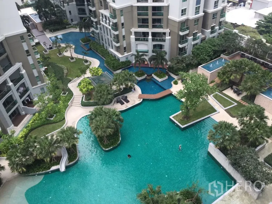 Condominium for rent in Huai Khwang, Bangkok - Aerial view of a resort-style lagoon pool with landscaped gardens, bridges and modern condominium towers.