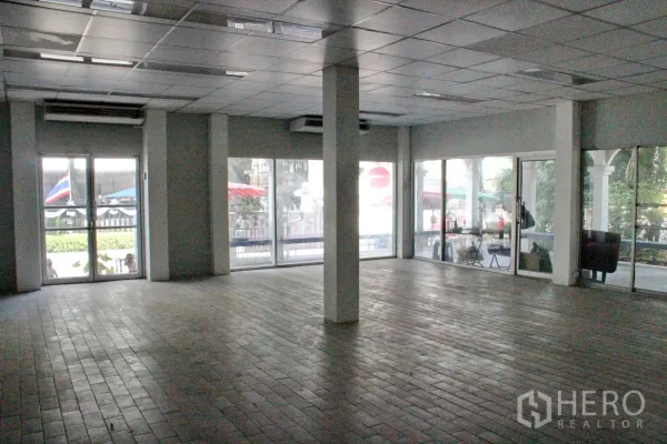 Home Office for rent in Khlong Toei, Bangkok - Large open-plan office hall with tiled floor, grid ceiling, columns and expansive glass doors and windows.