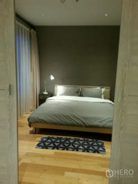 公寓 出租或出售在Khlong Toei, Bangkok - 卧室配木地板、双人床、床头灯和落地窗帘。