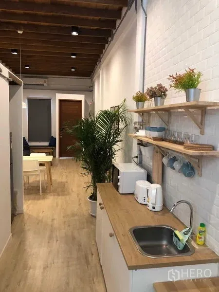 Detached House for rent in Phra Nakhon, Bangkok - Bright galley kitchen with wood countertop, open shelves, and plants leading toward the dining area.