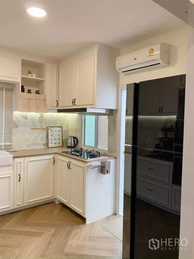 独立式住宅 出售在Sai Mai, Bangkok - 紧凑厨房，白色橱柜、燃气灶与黑色冰箱。