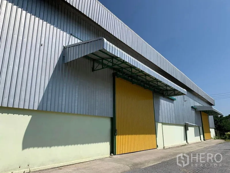 Warehouse for rent in Lat Krabang, Bangkok - Metal-clad warehouse facade in Lat Krabang with a large yellow sliding door and covered loading canopy under a clear blue sky.