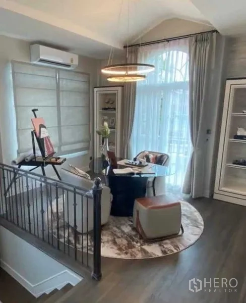 独立式住宅 出租在Bang Khen, Bangkok - 楼梯旁明亮会客区，圆形地毯与现代吊灯。