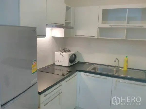 Condominium for rent in Watthana, Bangkok - Modern L-shaped kitchen with white cabinets, fridge, hob and microwave