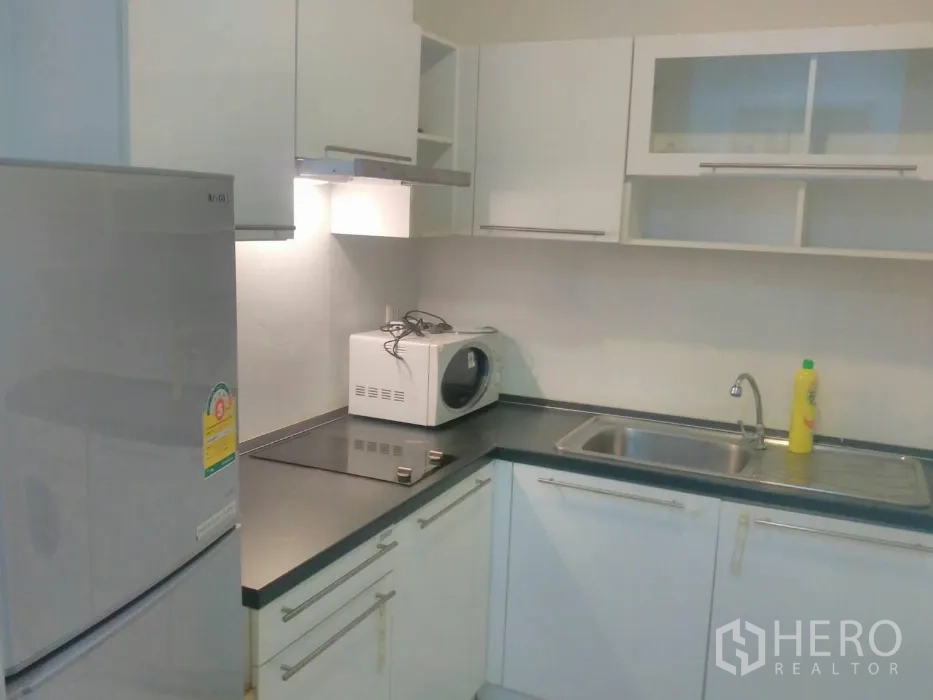 Condominium for rent in Watthana, Bangkok - Modern L-shaped kitchen with white cabinets, fridge, hob and microwave
