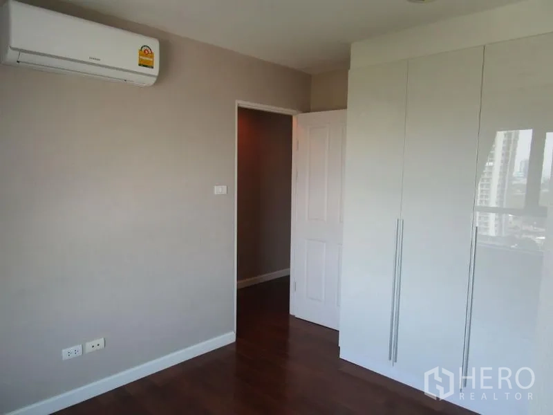 Condominium for sale in Huai Khwang, Bangkok - Bedroom with white built-in wardrobe, air conditioner, and wood flooring