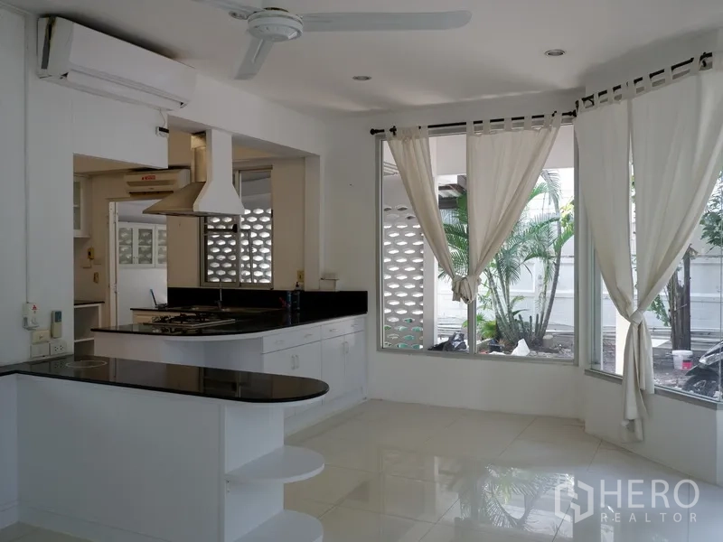 Detached House for rent in Khlong Toei, Bangkok - Corner kitchen with black stone countertops, white cabinetry and garden views.