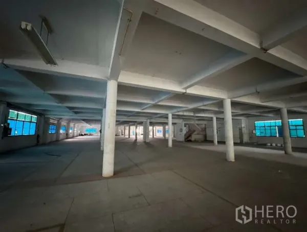 Home Office for sale in Bang Na, Bangkok - Large warehouse floor with white pillars, fluorescent lighting and blue-tinted windows.