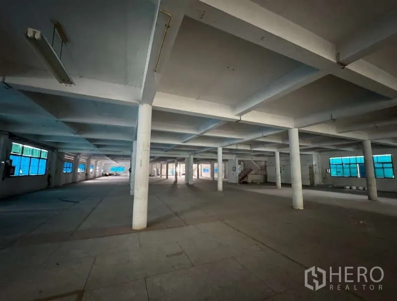 Home Office for sale in Bang Na, Bangkok - Large warehouse floor with white pillars, fluorescent lighting and blue-tinted windows.