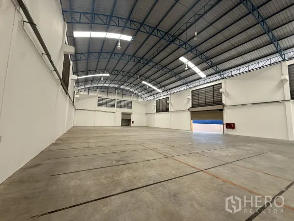 Warehouse for rent or sale in Bang Bo, Samut Prakan - Large warehouse bay showing roller shutters, louvered vents and wall‑mounted fire hose cabinet.