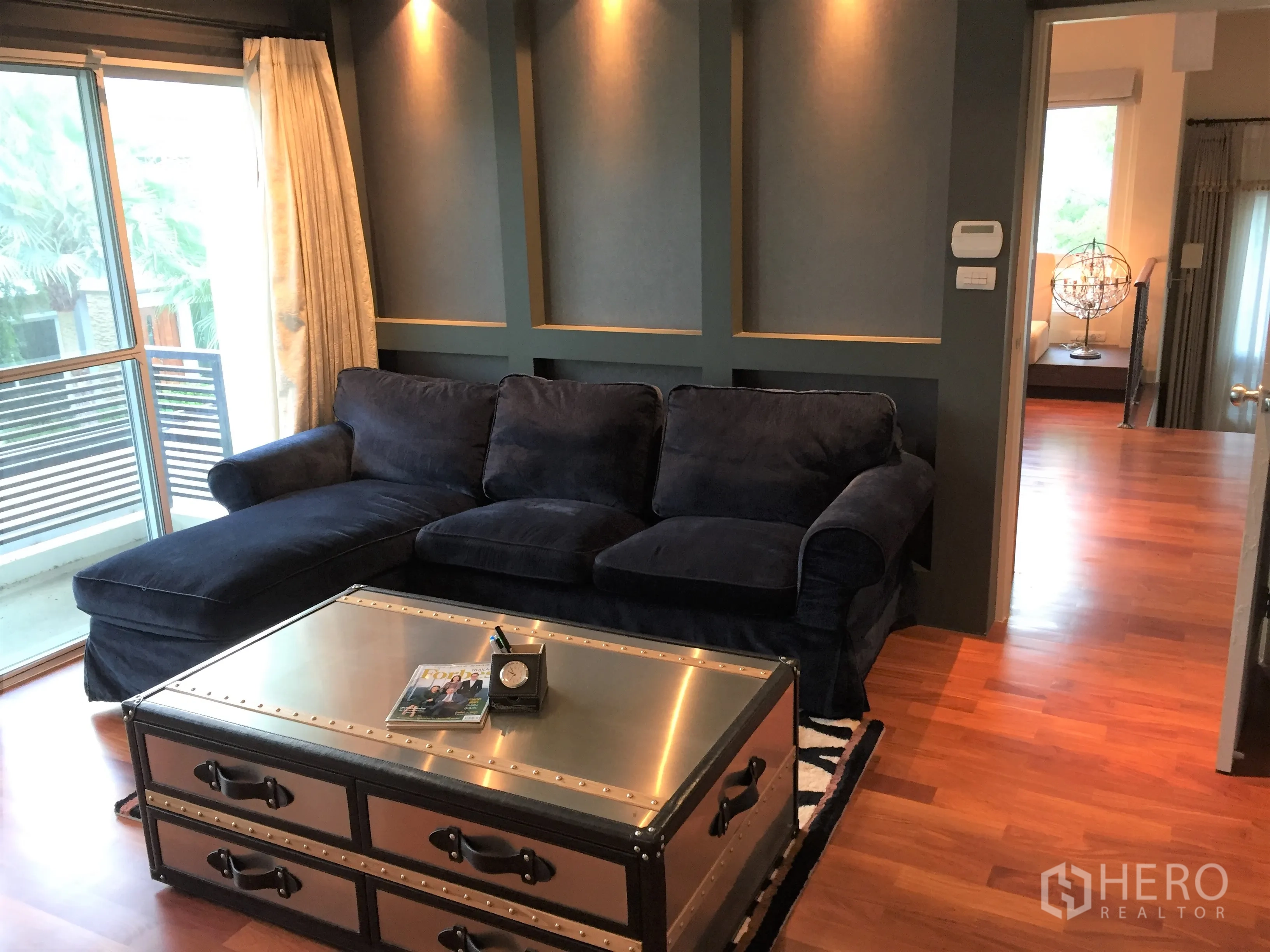 Detached House for sale in Saphan Sung, Bangkok - Cozy family lounge with navy sectional sofa, metal trunk coffee table and access to a balcony.