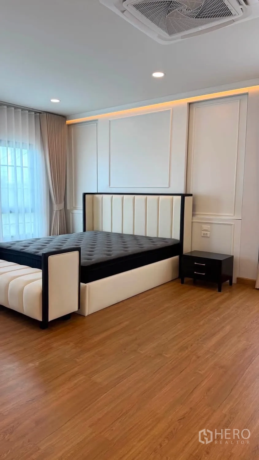 บ้านเดี่ยว for rent or sale in Bang Phli, Samut Prakan - ห้องนอนกว้างพร้อมเตียงบุผ้า ม้านั่งปลายเตียง โต๊ะข้าง และพื้นไม้