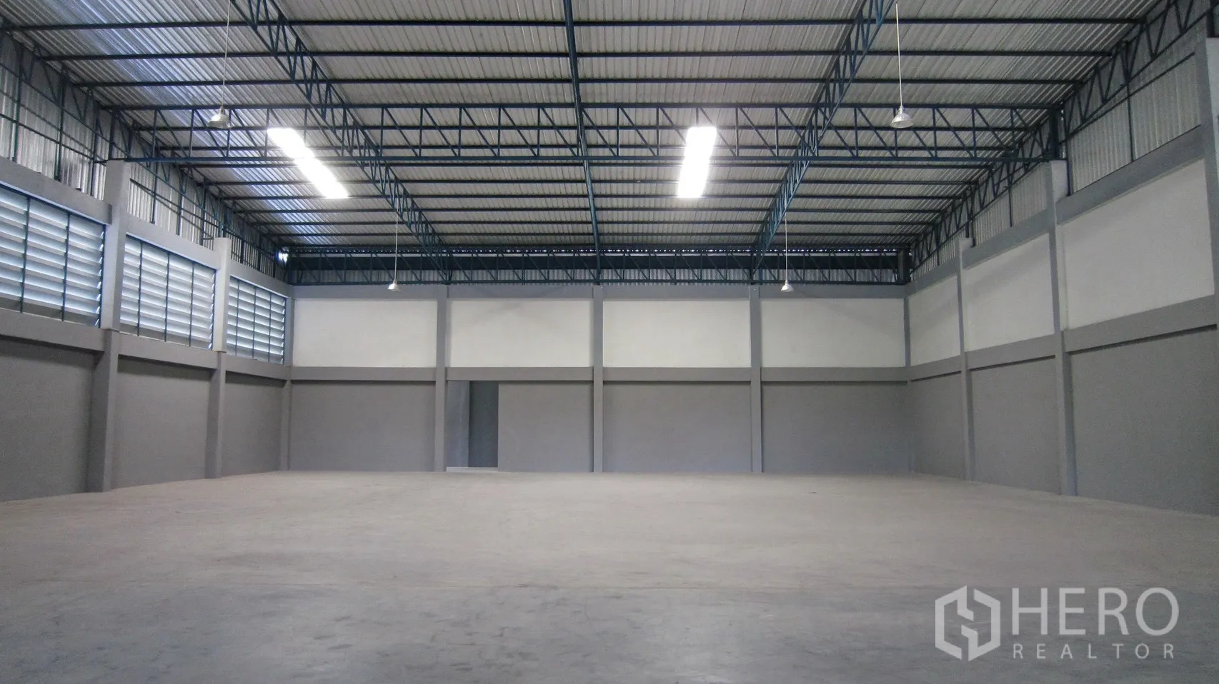 Warehouse for rent in Bang Sao Thong, Samut Prakan - Large open storage hall beneath a high roof with hanging lights and louvred vents.
