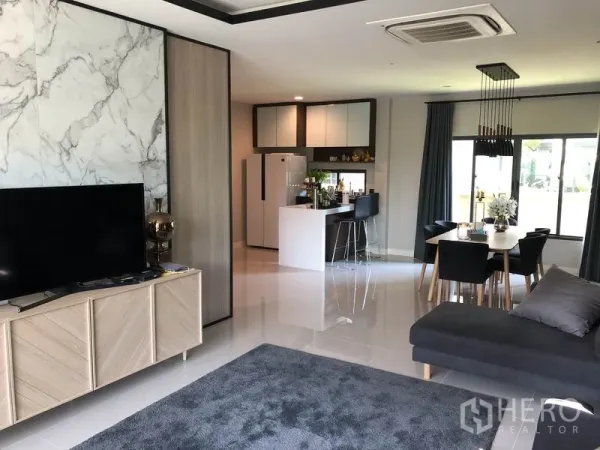Detached House for rent in Bang Kapi, Bangkok - Open-plan living area with marble feature wall, sofa, island kitchen and dining table by large windows.