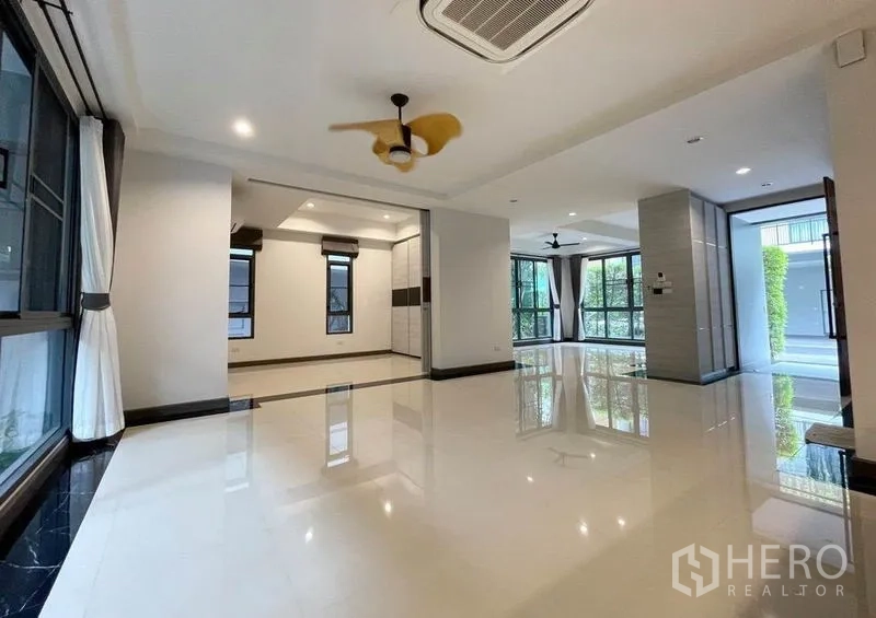 Detached House for rent in Bang Na, Bangkok - Spacious open-plan living area with glossy floors, large windows and ceiling fans.