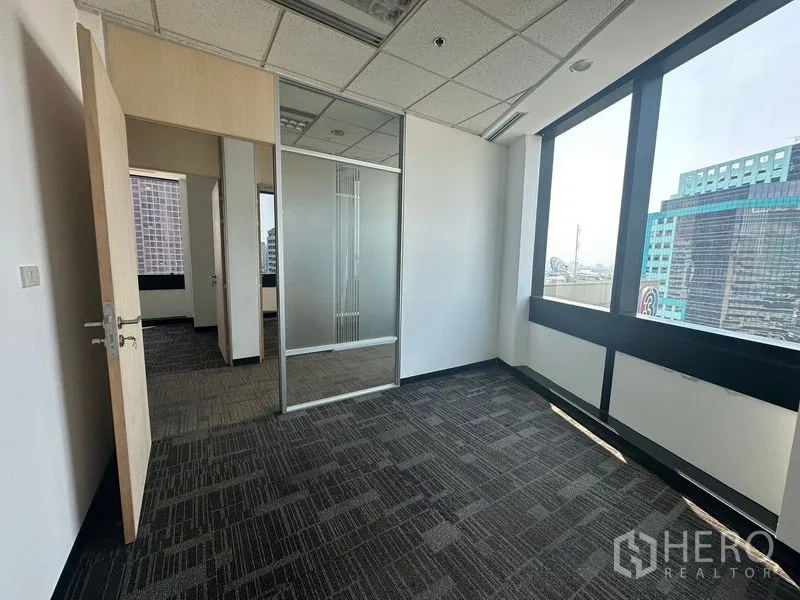 办公空间 出租在Khlong Toei, Bangkok - 铺地毯的独立办公室，玻璃隔断与大窗俯瞰城市。