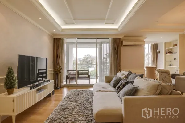 คอนโด ให้เช่าหรือขายในWatthana, Bangkok - ห้องนั่งเล่นสว่างด้วยโซฟาขนาดใหญ่ ตู้ทีวี และประตูกระจกบานเลื่อนออกสู่ระเบียงวิวต้นไม้