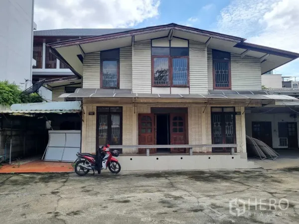 Detached House for rent or sale in Watthana, Bangkok - Front facade of the two-story house with awnings, security grilles and wide driveway.