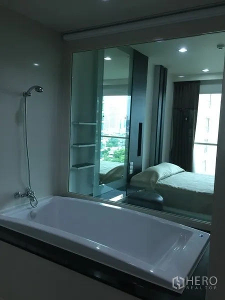 Condominium for rent in Pathum Wan, Bangkok - Bathroom with soaking bathtub and glass wall looking into the bedroom and city beyond.