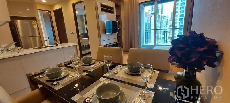 Condominium for rent in Ratchathewi, Bangkok - Dining area set for four beside balcony doors with an urban outlook.