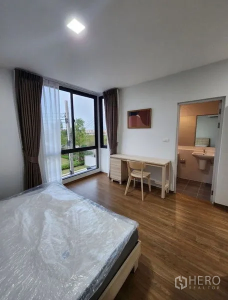 Townhouse for rent in Bang Phli, Samut Prakan - Master bedroom with floor-to-ceiling windows, work desk, and ensuite bathroom overlooking greenery.