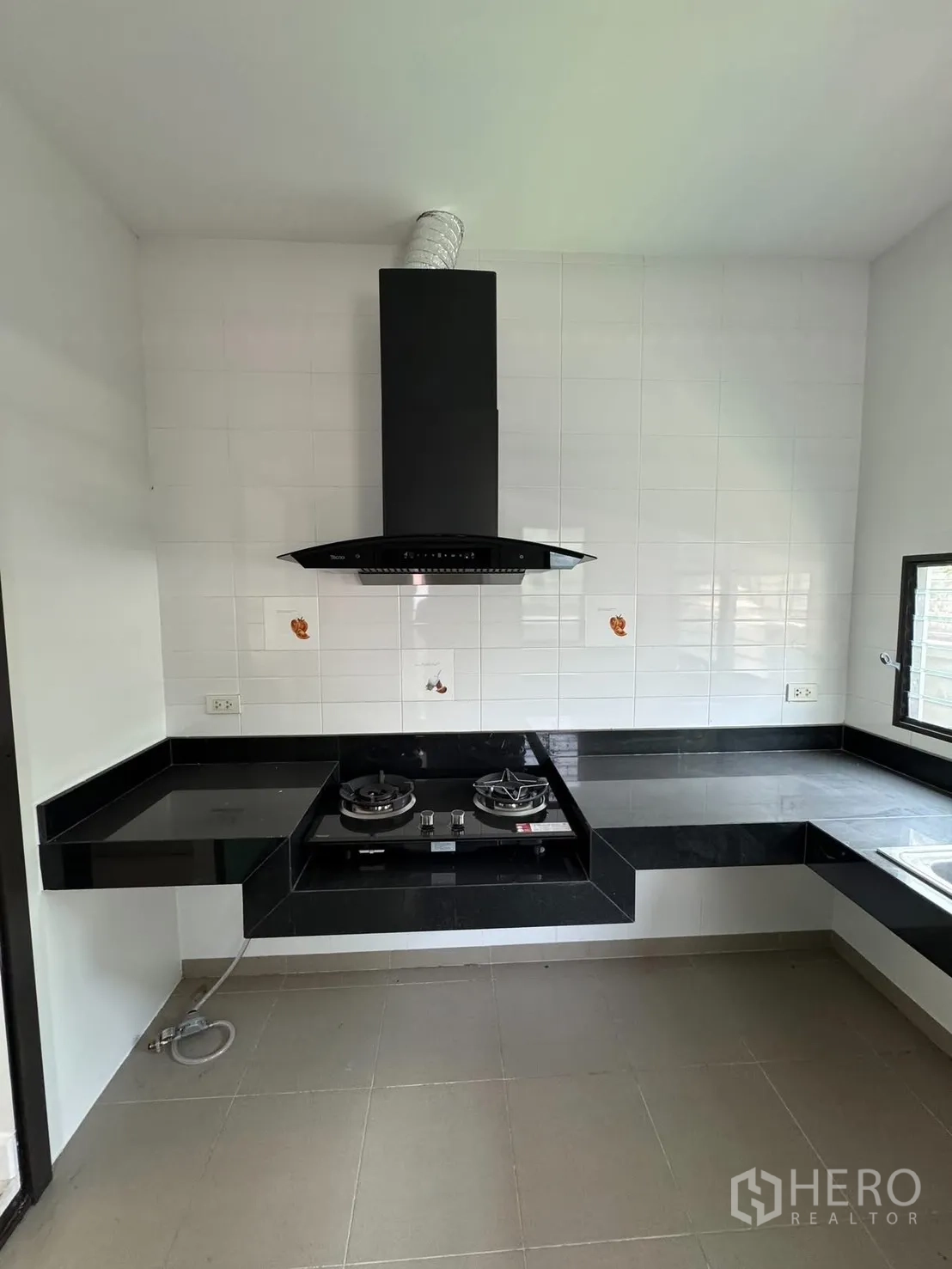 Detached House for rent in Prawet, Bangkok - Kitchen with black countertops, gas hob and chimney hood.