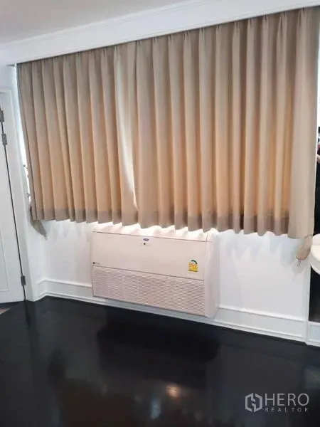 Condominium for rent in Sathon, Bangkok - Wall-mounted air conditioner beneath full-length curtains in living area.