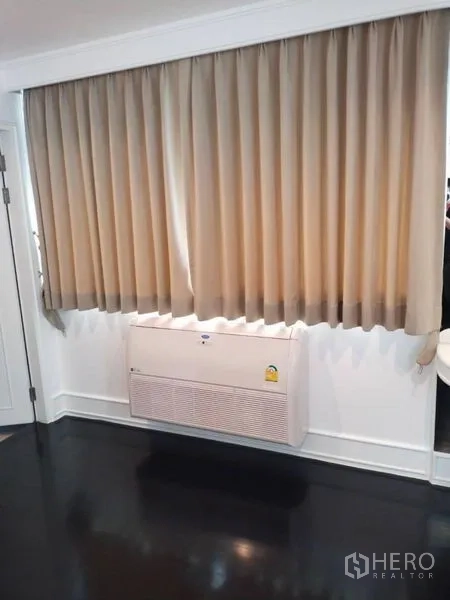 Condominium for rent in Sathon, Bangkok - Wall-mounted air conditioner beneath full-length curtains in living area.