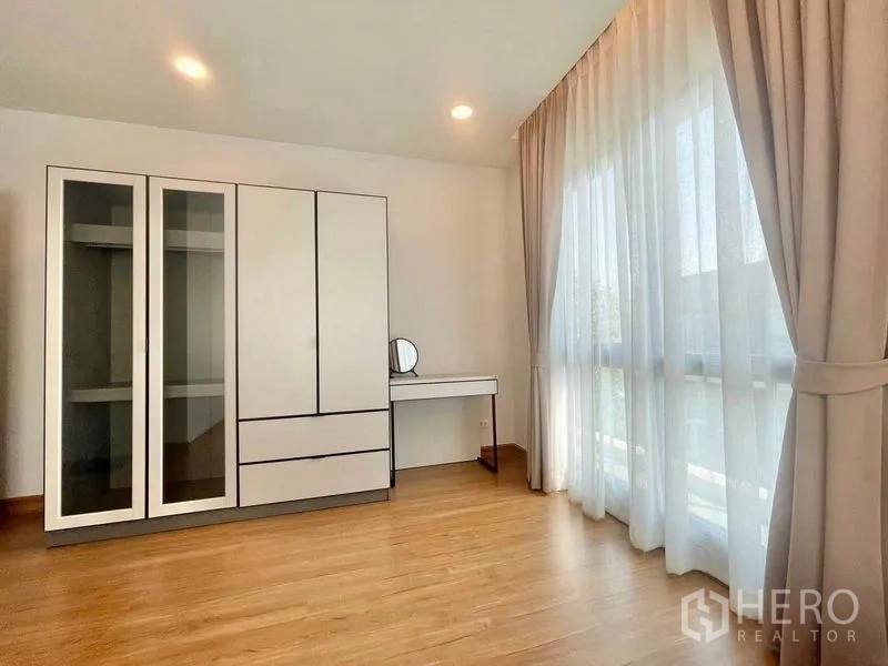 Detached House for rent in Bang Phli, Samut Prakan - Bright bedroom with floor-to-ceiling sheer curtains, wardrobe and vanity on wood flooring.