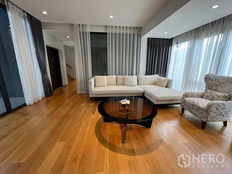 Detached House for sale in Suan Luang, Bangkok - Corner family lounge with L-shaped sofa, armchair and floor-to-ceiling curtains.