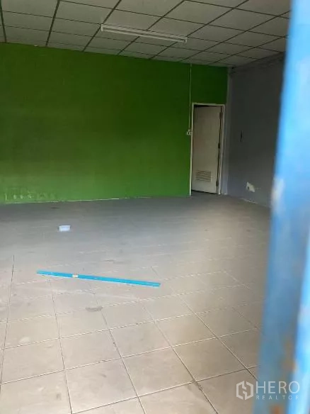 Factory for rent in Bang Phli, Samut Prakan - Simple office room with tiled floor, green accent wall and fluorescent ceiling lights.