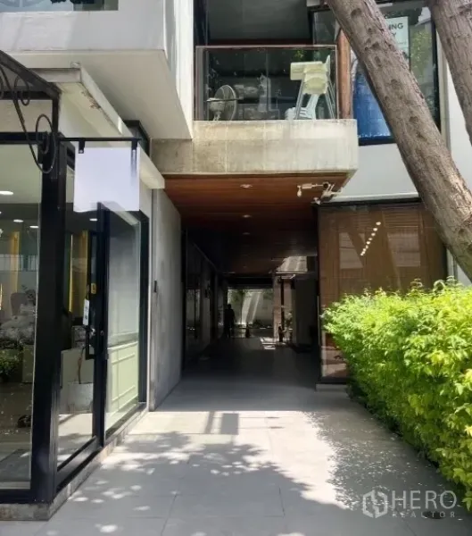 零售空间 出租在Watthana, Bangkok - 带绿篱的遮荫零售通道，现代玻璃店面与木质吊顶。