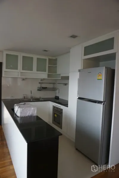 คอนโด ให้เช่าในWatthana, Bangkok - ครัวรูปตัวแอล เคาน์เตอร์หินสีดำ ตู้สีขาว ตู้เย็นสแตนเลส และเตาอบบิลท์อิน