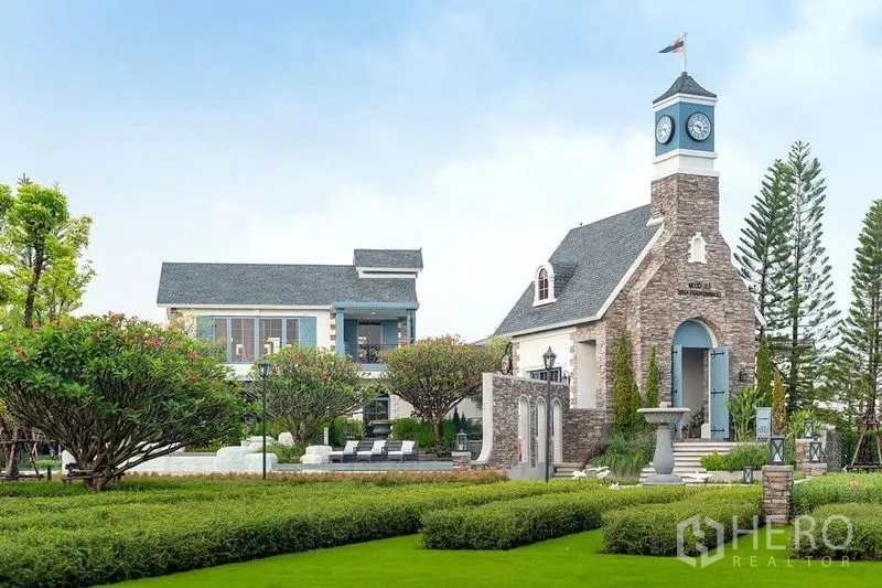 Detached House for rent or sale in Prawet, Bangkok - Community clubhouse with a clock tower, landscaped gardens and poolside seating.