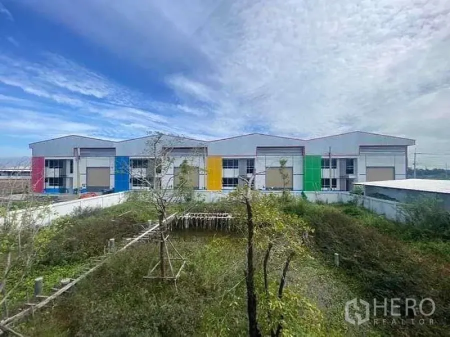 Warehouse for rent in Bang Phli, Samut Prakan - Row of colorful warehouse units in a secure compound beside landscaped greenery.
