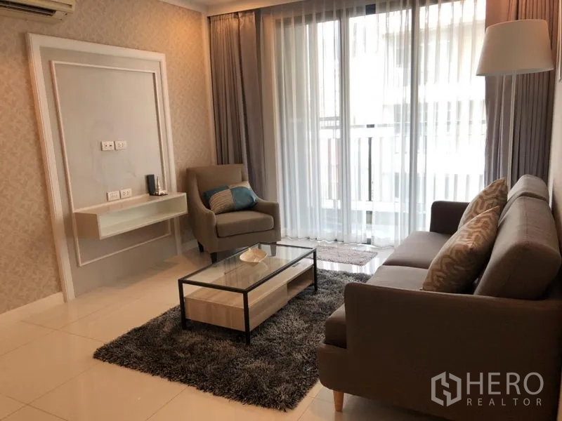 Condominium for rent in Watthana, Bangkok - Contemporary living room with sofa and armchair, shag rug, glass coffee table, and balcony doors with sheer curtains.