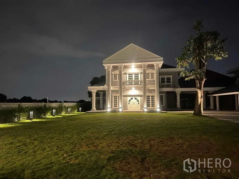 Detached House for sale in Bang Na, Bangkok - Grand neoclassical two-storey house illuminated at night with a wide lawn in front.