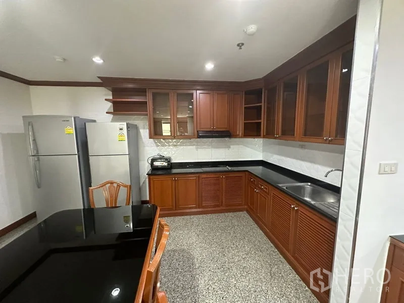 คอนโด ให้เช่าในWatthana, Bangkok - ครัวปิดพร้อมตู้ไม้บิวท์อิน เคาน์เตอร์หินสีดำ ตู้เย็นสองประตู และโต๊ะทานข้าว