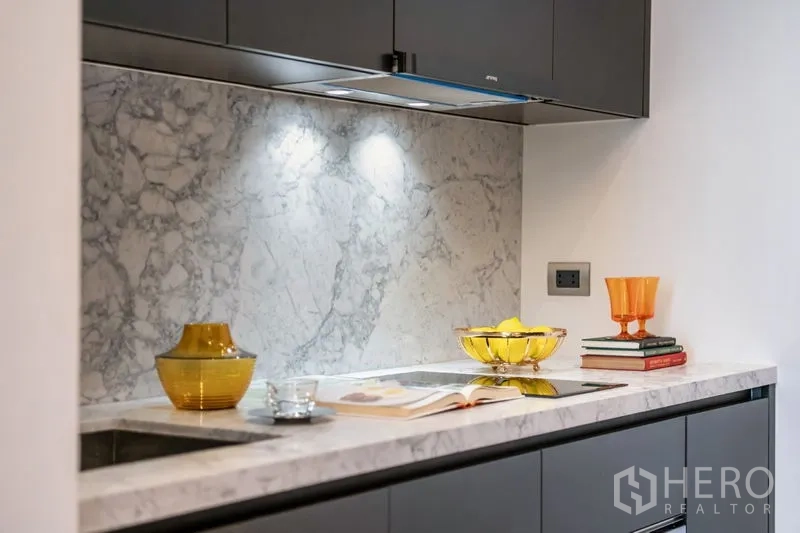 คอนโด ให้เช่าในWatthana, Bangkok - ภาพใกล้ของท็อปหินอ่อน เตาไฟฟ้า และแก้วสีอำพันใต้ไฟส่องสว่าง