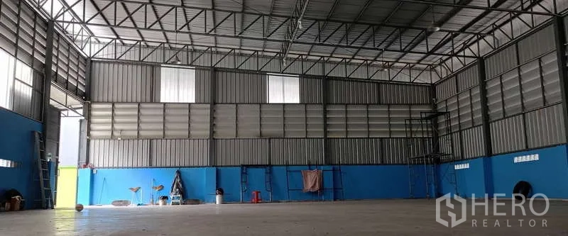 Warehouse for rent in Mueang Samut Sakhon, Samut Sakhon - Spacious high-ceiling warehouse interior with steel trusses, ventilated panels and blue walls over a polished concrete floor.