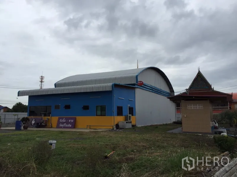 Warehouse for rent in Mueang Pathum Thani, Pathum Thani - Side elevation of the blue-and-yellow warehouse with arched roof and lawn area.