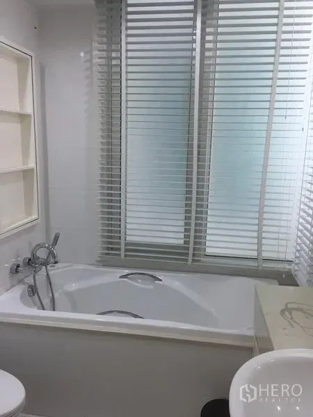 คอนโด ให้เช่าในKhlong Toei, Bangkok - ห้องน้ำโทนขาว มีอ่างอาบน้ำ ฝักบัวแบบมือถือ อ่างล้างหน้า ชั้นวาง และมู่ลี่หน้าต่าง