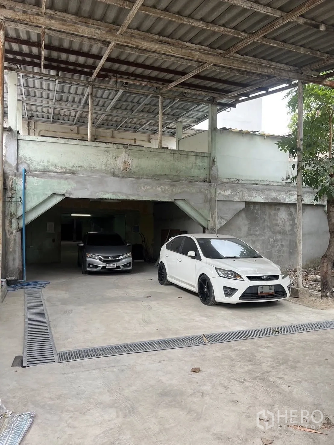 Warehouse for rent in Phra Pradaeng, Samut Prakan - Front parking and loading space under a roof canopy with floor drains and vehicle access.