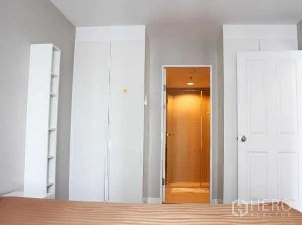 Condominium for rent in Huai Khwang, Bangkok - Master bedroom with built-in wardrobes and an en-suite bathroom featuring a glass shower.