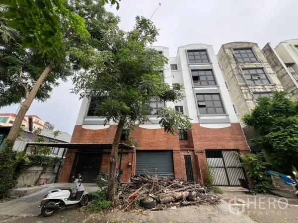 店屋 出租在Phra Khanong, Bangkok - 四层店屋，红砖基座与黑框大窗，门前绿树成荫。