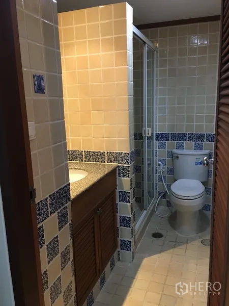 Condominium for rent in Pathum Wan, Bangkok - Second bathroom with beige and blue tiles, enclosed shower, and toilet.