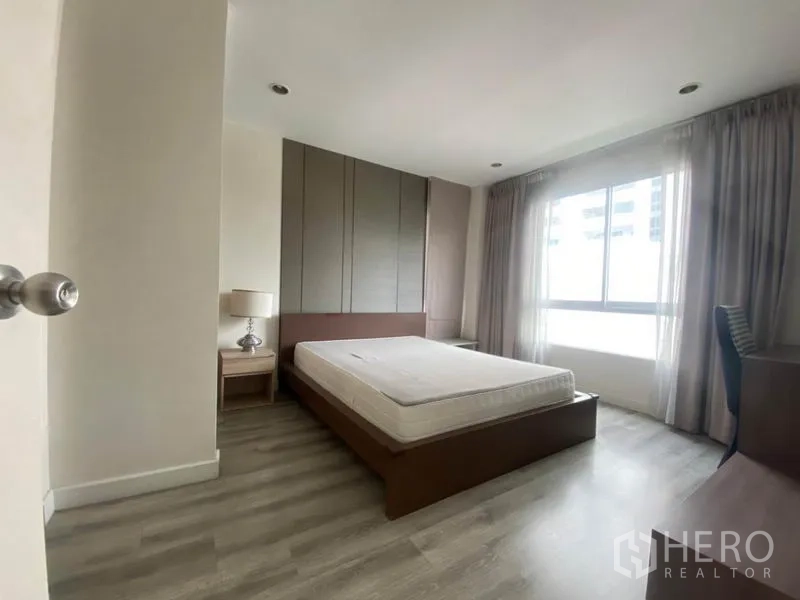 Condominium for rent in Watthana, Bangkok - Bright bedroom with large window, bed frame, bedside table, and neutral decor.